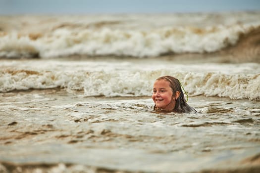 Little girl playing with waves in the sea. Kid playfully splashing in waves. Child jumping in sea. Vacations on the beach. Water splashes. Fun and play during summer vacation. Travel concept