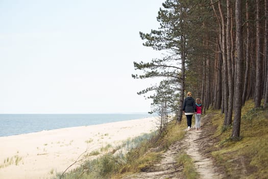 Woman and her daughter walking along seashore and forest. Family spending vacations at sea. Summer trip. Enjoying free time. Leisure time close to nature. Travel concept