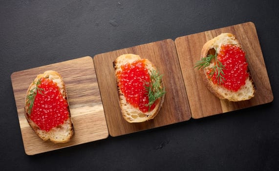 Red caviar on slices of white wheat bread on a black table, concept of luxury and gourmet cuisine, top view
