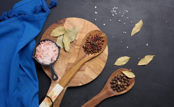 Peppercorns and salt in a wooden spoon on a black table, top view