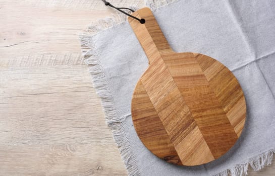 Empty round oak board and gray towel on a wooden table, top view