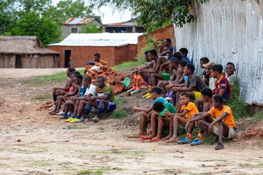 BEKOPAKA, MADAGASCAR - NOVEMBER 6, 2022: Soccer fans sitting on the ground and watching a local match between two teams from the village. The match is part of a sunday village festival.