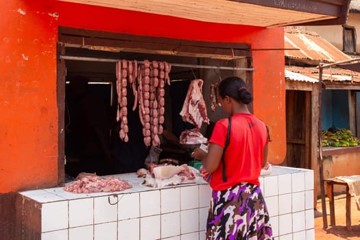 Mandoto, Madagascar - November 9th, 2022: A woman buys meat from a street butchery in Mandoto, Madagascar. The shop displays sausages on a stand that hang in the heat of the day.