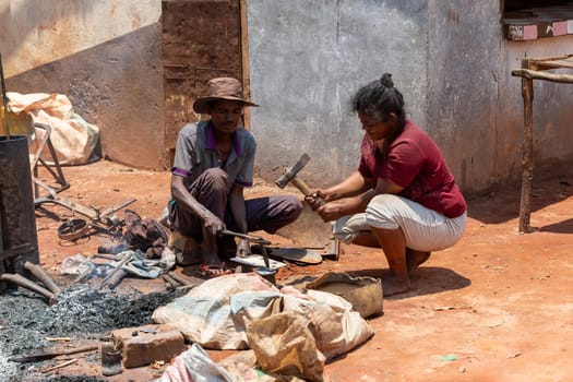 Mandoto, Madagascar - November 9th 2022 - A Malagasy couple runs a blacksmithing business in Mandoto. A Malagasy blacksmith works on iron while his wife operates the bellows in their workshop.