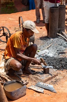 Mandoto, Madagascar - November 9th 2022 - A Malagasy couple runs a blacksmithing business in Mandoto. A Malagasy blacksmith works on iron while his wife operates the bellows in their workshop.