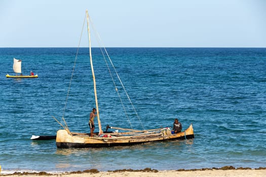 ANAKAO, MADAGASCAR - NOVEMBER 24, 2022: Mans using outrigger canoe carved from tree to transport goods from Toliara to Anakao. Malagasy traditional boat with a single outrigger, is used for centuries.