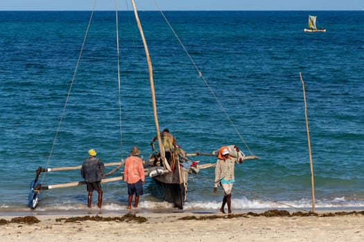 ANAKAO, MADAGASCAR - NOVEMBER 24, 2022: Mans unloading the outrigger carved canoe to transport goods from Toliara to Anakao. Malagasy traditional boat with a single outrigger, is used for centuries.