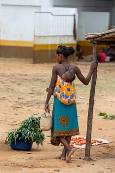 Bekopaka, Madagascar - November 6, 2022: Malagasy woman walking down the street with a child on her back.