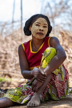 Belo Sur Tsiribihina, Madagascar - November 4. 2022: Malagasy woman in front of her hut with a traditionally painted face. Malagasy women paint their faces to protect their faces from the sun.