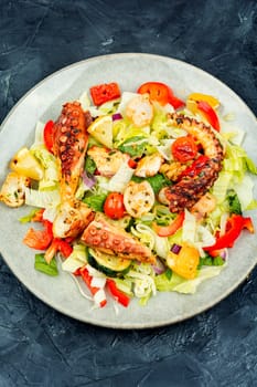 Tasty salad of fresh vegetables and octopus tentacles. Octopus salad on wooden background.