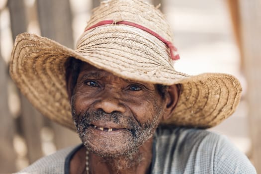 Miandrivazo, Madagascar - November 2nd 2022 - Elderly man wearing a straw hat and smiling. Senior man resting on the street.