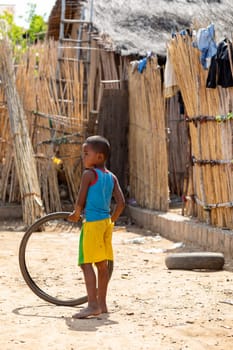 Miandrivazo, Madagascar - November 27th 2022: A young boy plays with an old bicycle tire while standing on a dirt road.