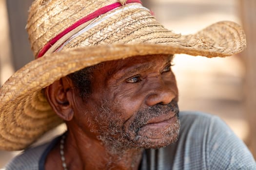 Miandrivazo, Madagascar - November 2nd 2022 - Elderly man wearing a straw hat and smiling. Senior man resting on the street.