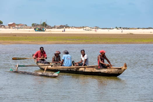 MORONDAVA, MADAGASCAR - NOVEMBER 22, 2022: Malagasy family in traditional wooden boat crossing River in Morondava, Madagascar.