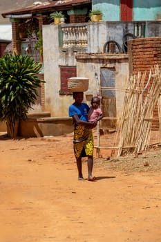 Vohitsoaka Ambalavao - November 6, 2022: Malagasy woman walking down the street with a child on her back.
