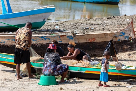 Morondava, Madagascar - November 3, 2022: Fisherman and woman repairing fishing nets at the estuaries of a river, canal Hellot. The woman has a traditionally Malagasy painted face