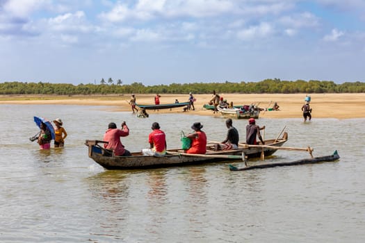MORONDAVA, MADAGASCAR - NOVEMBER 22, 2022: Malagasy family in traditional wooden boat crossing River in Morondava, Madagascar.