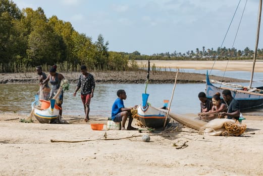 Morondava, Madagascar - November 3, 2022: Fisherman and woman repairing fishing nets at the estuaries of a river, canal Hellot. The woman has a traditionally Malagasy painted face