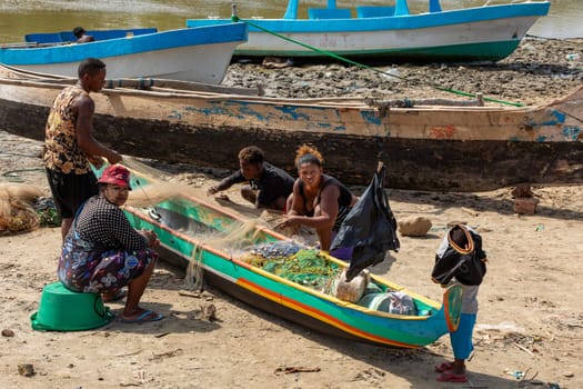Morondava, Madagascar - November 3, 2022: Fisherman and woman repairing fishing nets at the estuaries of a river, canal Hellot. The woman has a traditionally Malagasy painted face