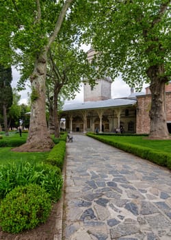 Istanbul, Turkey - May 11, 2023: Stone walkway surrounded by lush trees, leading to the Imperial Council building in the courtyard of Topkapi Palace