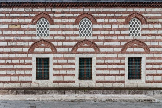 External wall of 16th century Selman Aga Mosque in Uskudar, Istanbul, Turkey. The wall is made of red brick and has two rows of arched perforated stucco and wrought iron windows