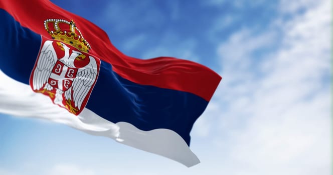 Serbia national flag waving in the wind on a clear day. Red, blue, and white bands, with Serbian coat of arms to the left of the center. 3d illustration render. Fluttering fabric. Selective focus
