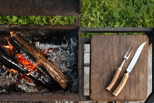 Top view of metal grill with burning log and fork and knife for steak