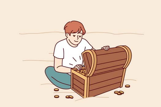 Treasure hunter boy found wooden chest with gold and is sitting on beach looking at prey. Little kid dreams of finding sunken treasure of pirates from middle ages and getting rich.