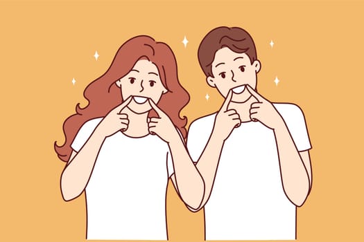 Happy man and woman smile broadly and raise fingers to mouths, recommending use of whitening toothpaste. Positive young couple showing positive attitude and fake joy at hearing news