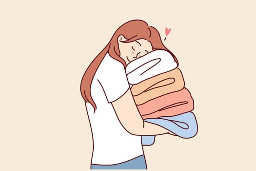Woman with multicolored clothes in hands, enjoys softness of towels after using fabric softener to wash. Girl holds clothes collected by charitable foundation to support poor people.