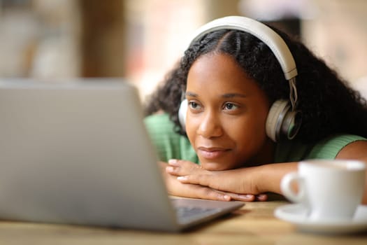 Black woman wearing headphone watching media on laptop in a restaurant terrace