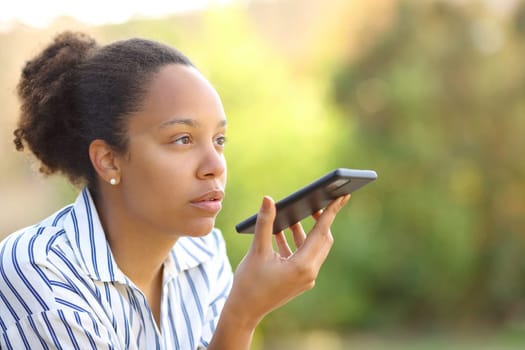 Black woman dictating text on phone usig voice recognition siting in a garden