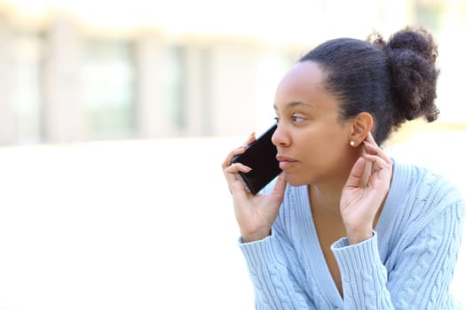 Black woman is talking on phone sitting in the street