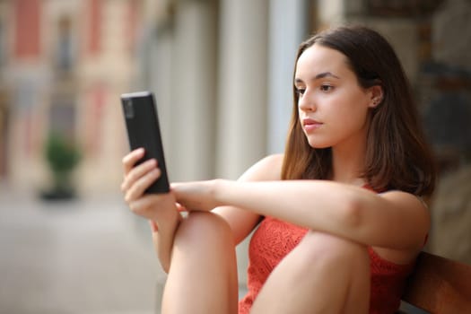 Serious woman checking phone content in the street