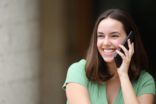Happy female is talking on phone looking at side in the street
