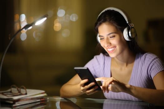 Happy woman with heaphone checking phone at night at home