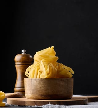 Raw long noodles made from white wheat flour in a wooden bowl on a black table