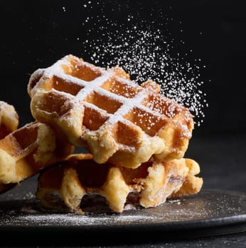 A stack of baked Belgian waffles sprinkled with powdered sugar