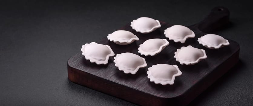 Raw frozen stuffed dumplings on a wooden cutting board on a dark concrete background