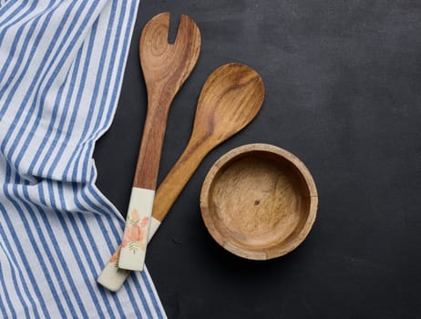 Empty bowl and wooden spoons on a black table, top view
