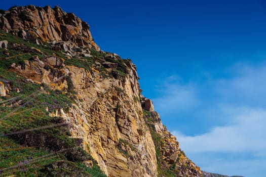 Beautiful scenic view of high rock mountain cliff peak covered with green grass, trees, bushes on background of blue turquoise sky. Landscape, nature, summer, tourism, mountaineering, advertisement.