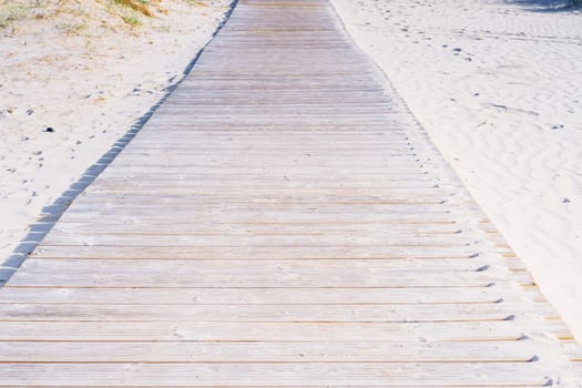 Wooden pathway road boardwalk surrounded by sand with footprints to beach sea ocean on sunny summer day. Summertime, holiday, vacation, travelling, nature, landscape, seashore, coastline, tourism.