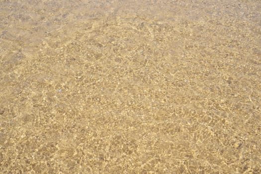Top view of transparent clean water of sea ocean. Yellow sand seen through water. Sun rays reflecting on waves. Summer, holidays, seascape, vacation, coastline, seashore, seaside, travelling, tourism.