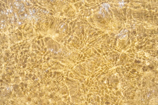 Top view of transparent clean water of sea ocean. Yellow sand seen through water. Sun rays reflecting on waves. Summer, holidays, seascape, vacation, coastline, seashore, seaside, travelling, tourism.
