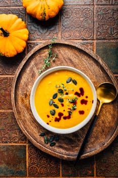 Pumpkin soup with pumpkin seeds  and pumpkin seed oil served in bowl on rustic kitchen table