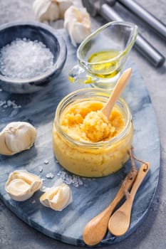 Homemade garlic paste in a jar with peeled garlic, salt, crusher and garlic heads.