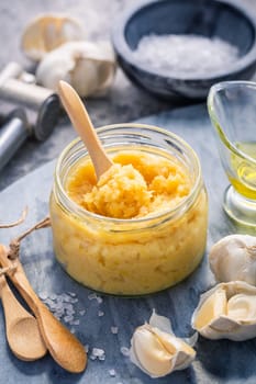 Homemade garlic paste in a jar with peeled garlic, salt, crusher and garlic heads.