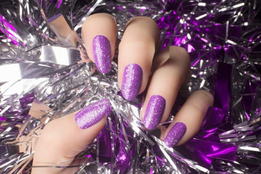 Female hand with glittered purple nails is holding silver decoration, manicure concept.