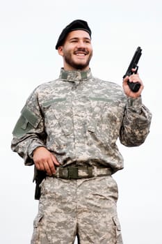 The smiling army soldier in military uniform is holding a pistol in hand on white background.