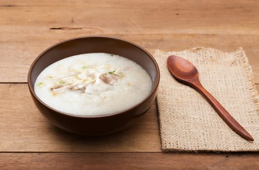 Traditional chinese porridge rice gruel in brown bowl with wooden spoon on wood table